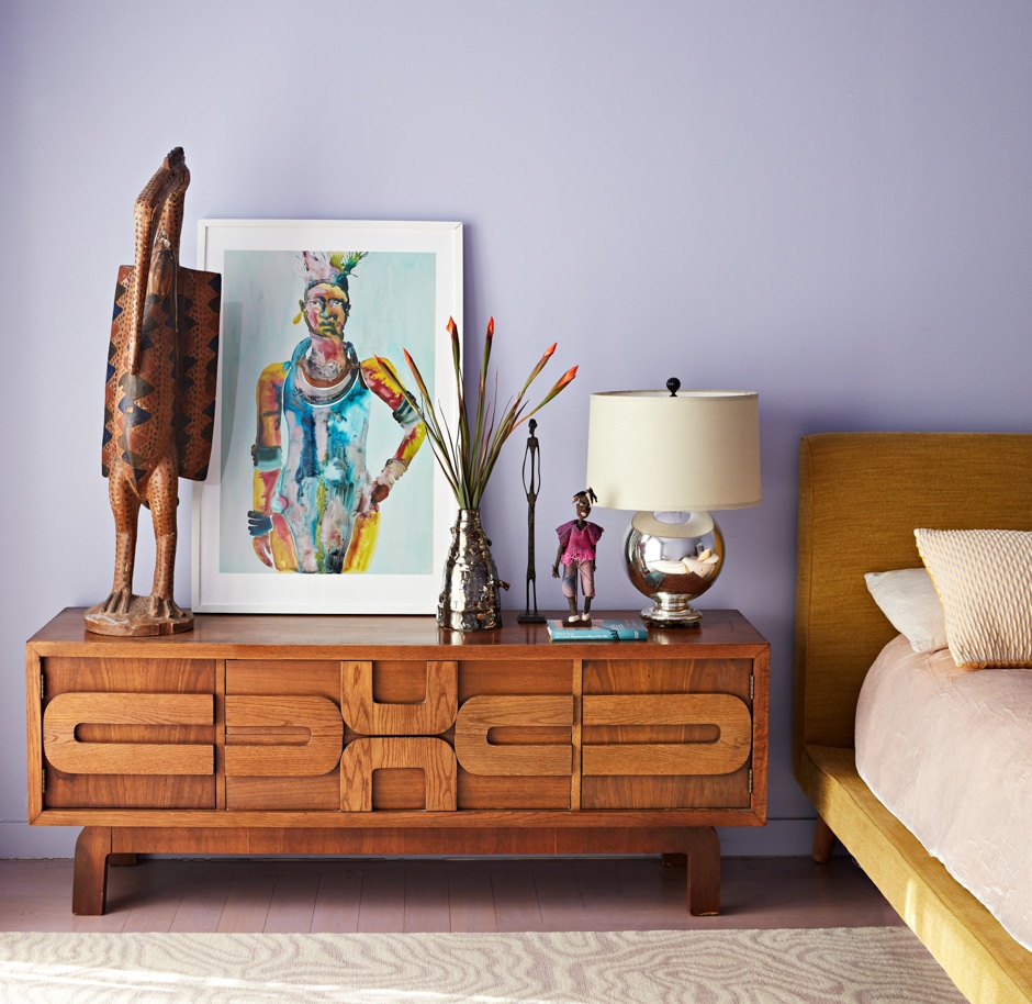 wooden bedside table with art on it and lavender walls