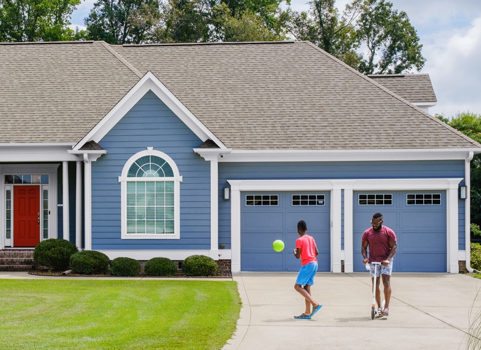 son and father playing in driveway of blue exterior home