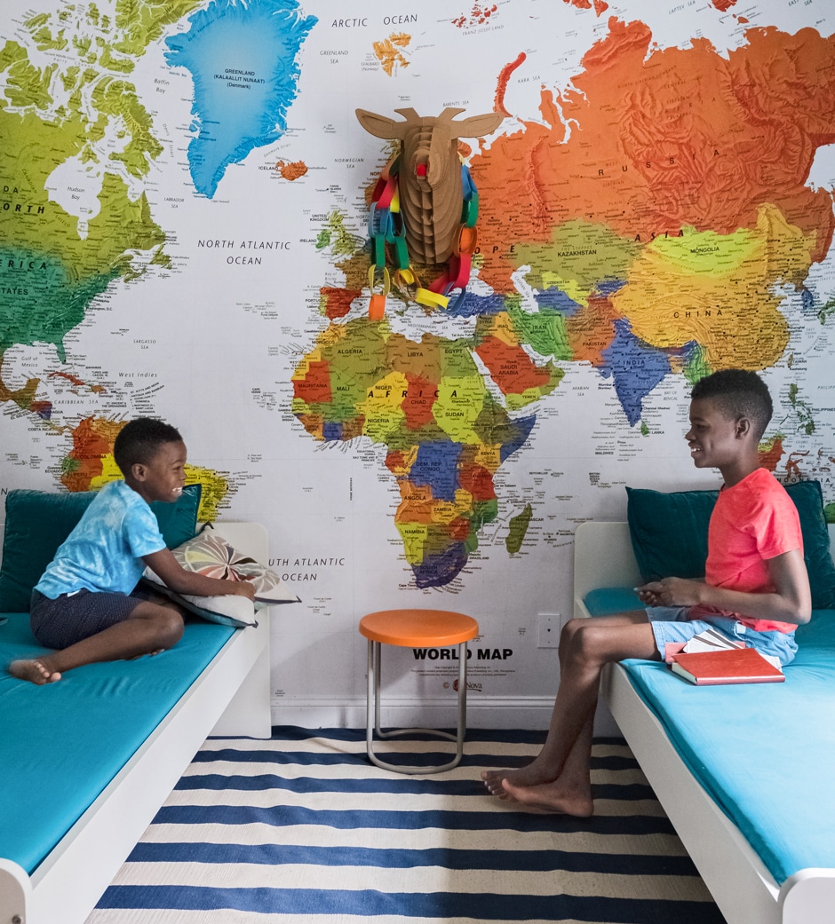 boys sitting in bedroom with twin beds and giant map mural wall