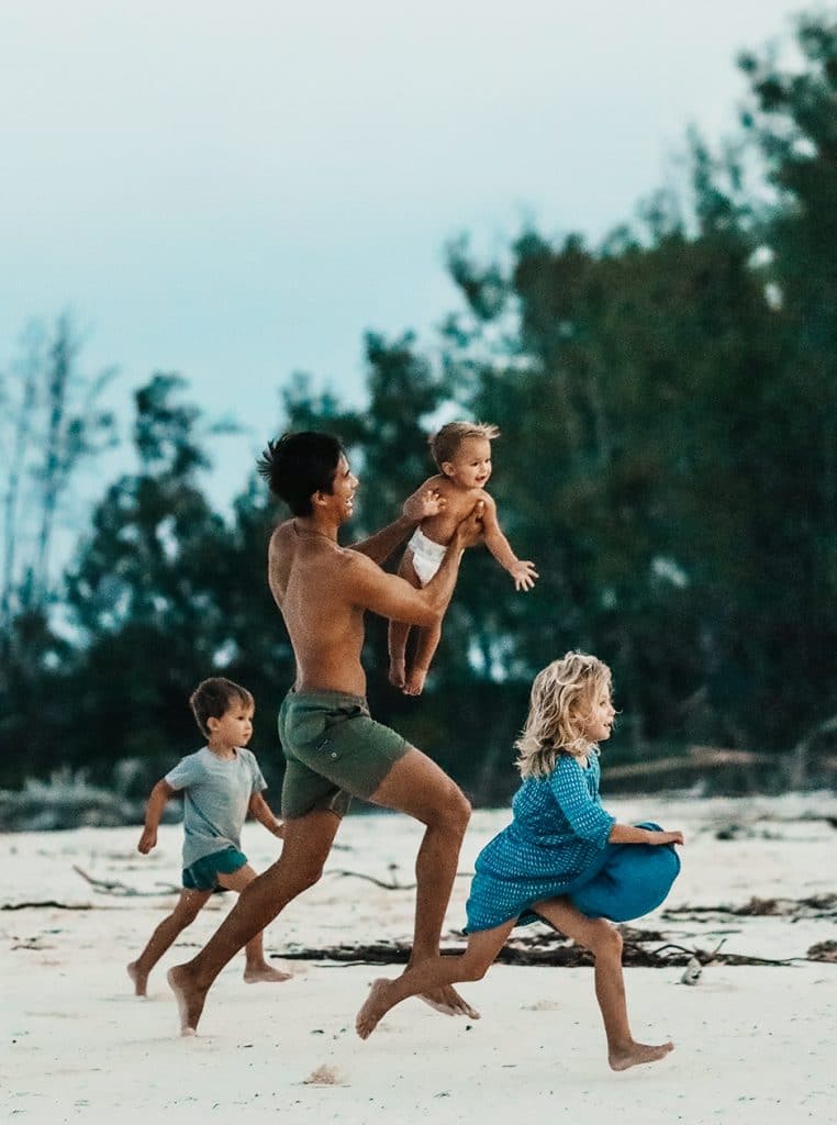 father running on beach with kids