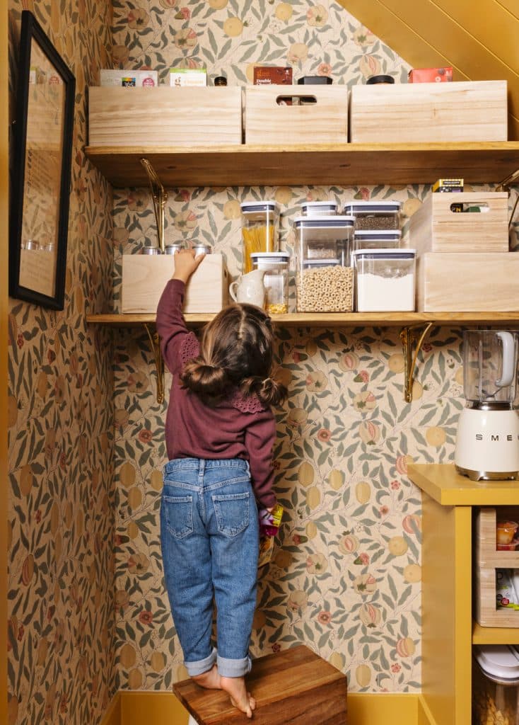 girl standing on booster in wallpapered pantry