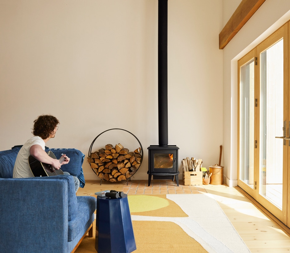 man sitting on couch playing guitar in room with wood burning stove