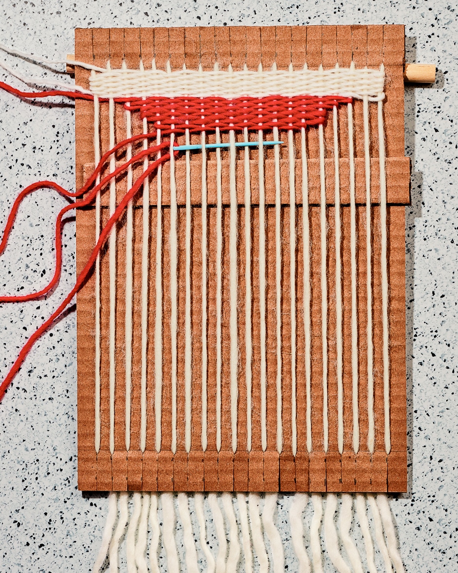 threading red and white yarn through cardboard loom