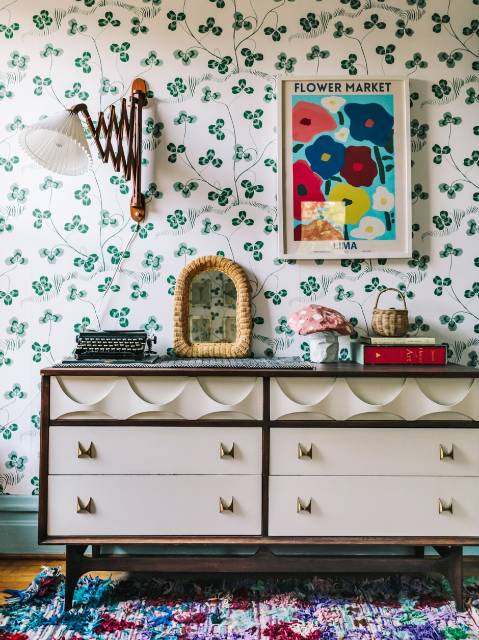 wallpapered guest room with dresser and art work