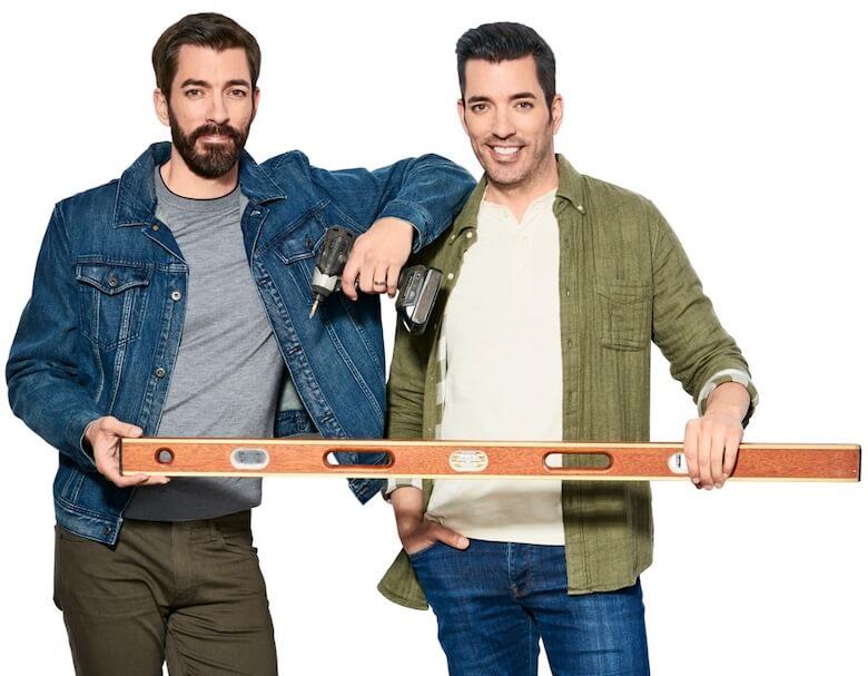 Drew and Jonathan Scott stand side by side holding a level together