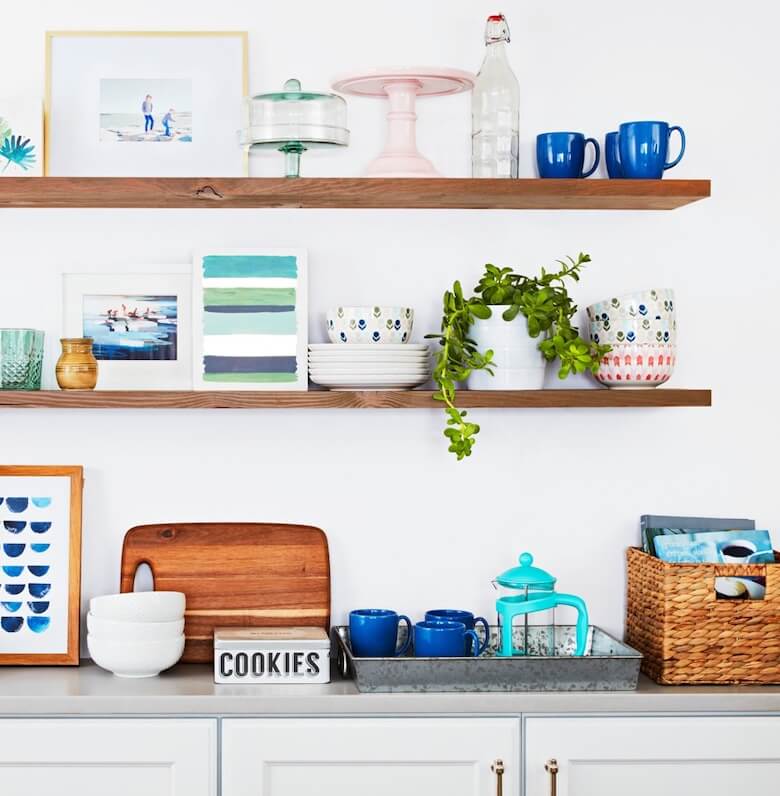 Wooden floating shelves over a counter hold dishes, decor, and plants