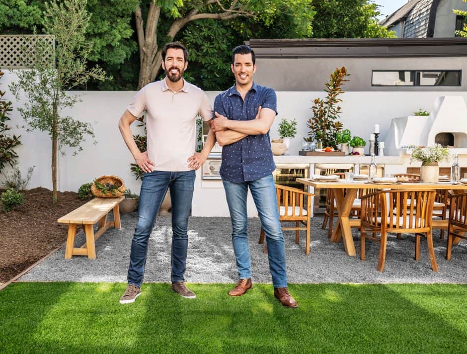 Scott brothers standing in a beautifully designed outdoor patio with a dining area, greenery, and wooden furniture