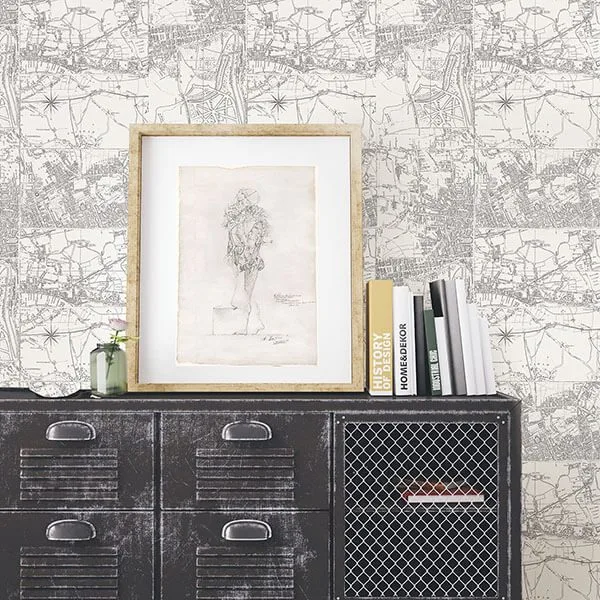 Black metal cabinet with a framed sketch, books, and a vase against a vintage map wallpaper