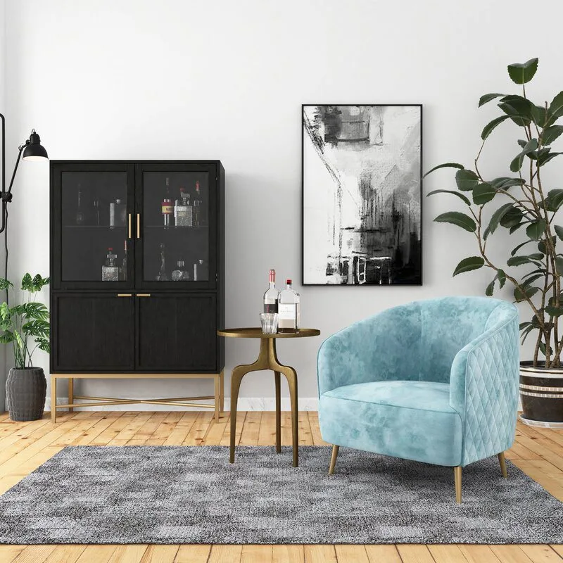 Living area with a blue velvet chair, gold table, black cabinet, abstract art, and greenery on a wood floor with a gray rug