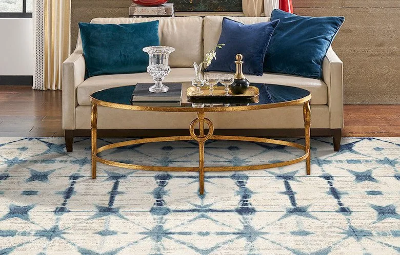 Luxurious living room with beige sofa, blue velvet pillows, gold coffee table, and patterned area rug