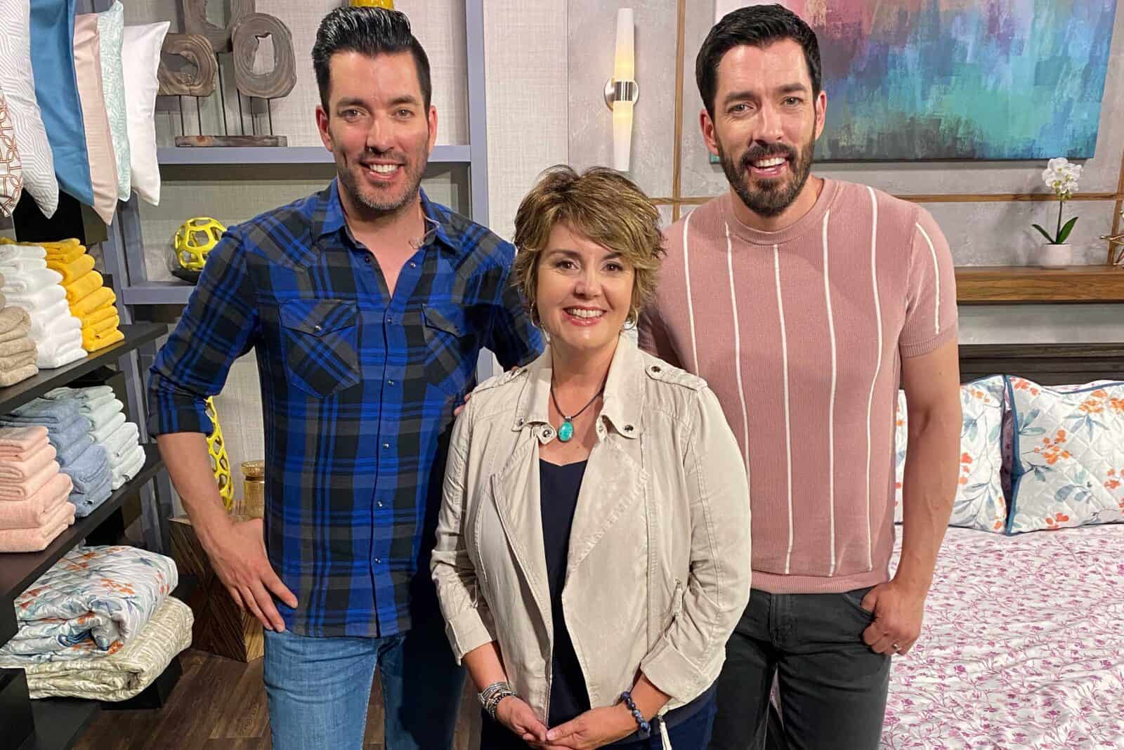 Scott brothers and a woman posing together in a home decor setting with folded towels and bedding in the background