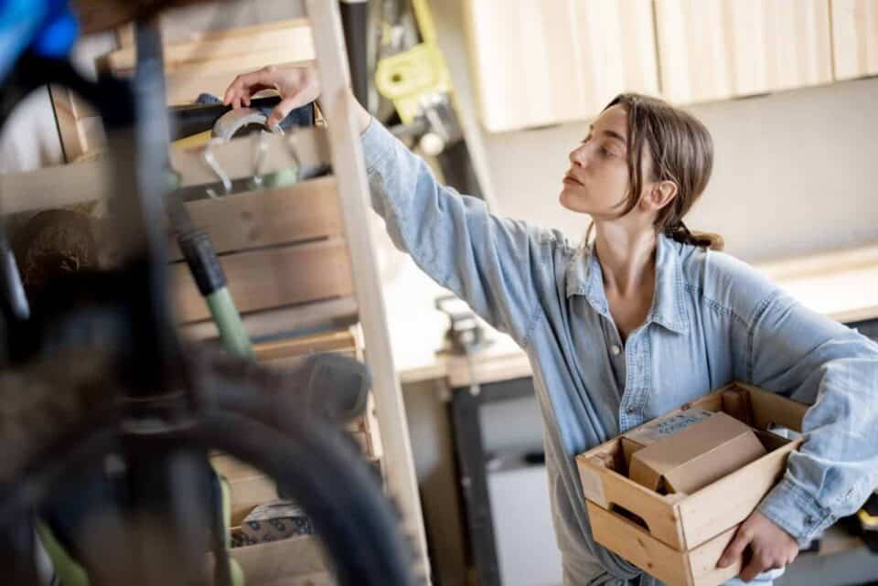 garage storage ideas to keep clutter off the floor, woman arranging her garage neatly