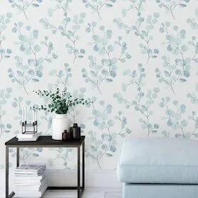Light blue floral wallpaper behind a black side table with a white vase and a light blue ottoman