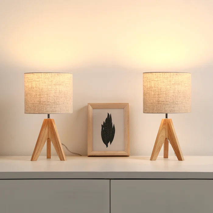 Two wooden table lamps with beige shades and a framed leaf art piece between them