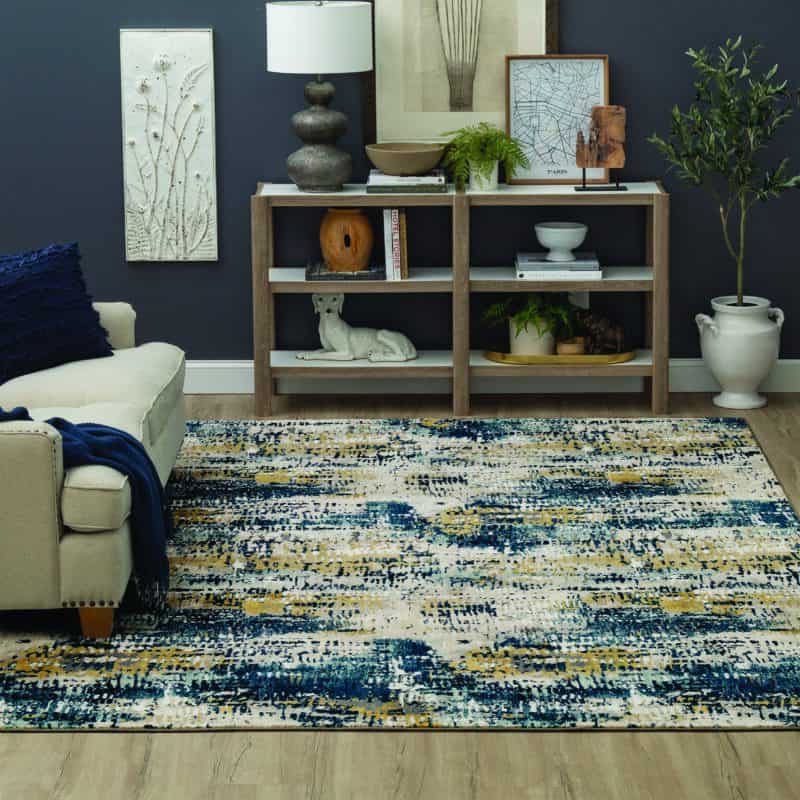 Cozy living room with a beige sofa, colorful rug, modern bookshelf, and plants