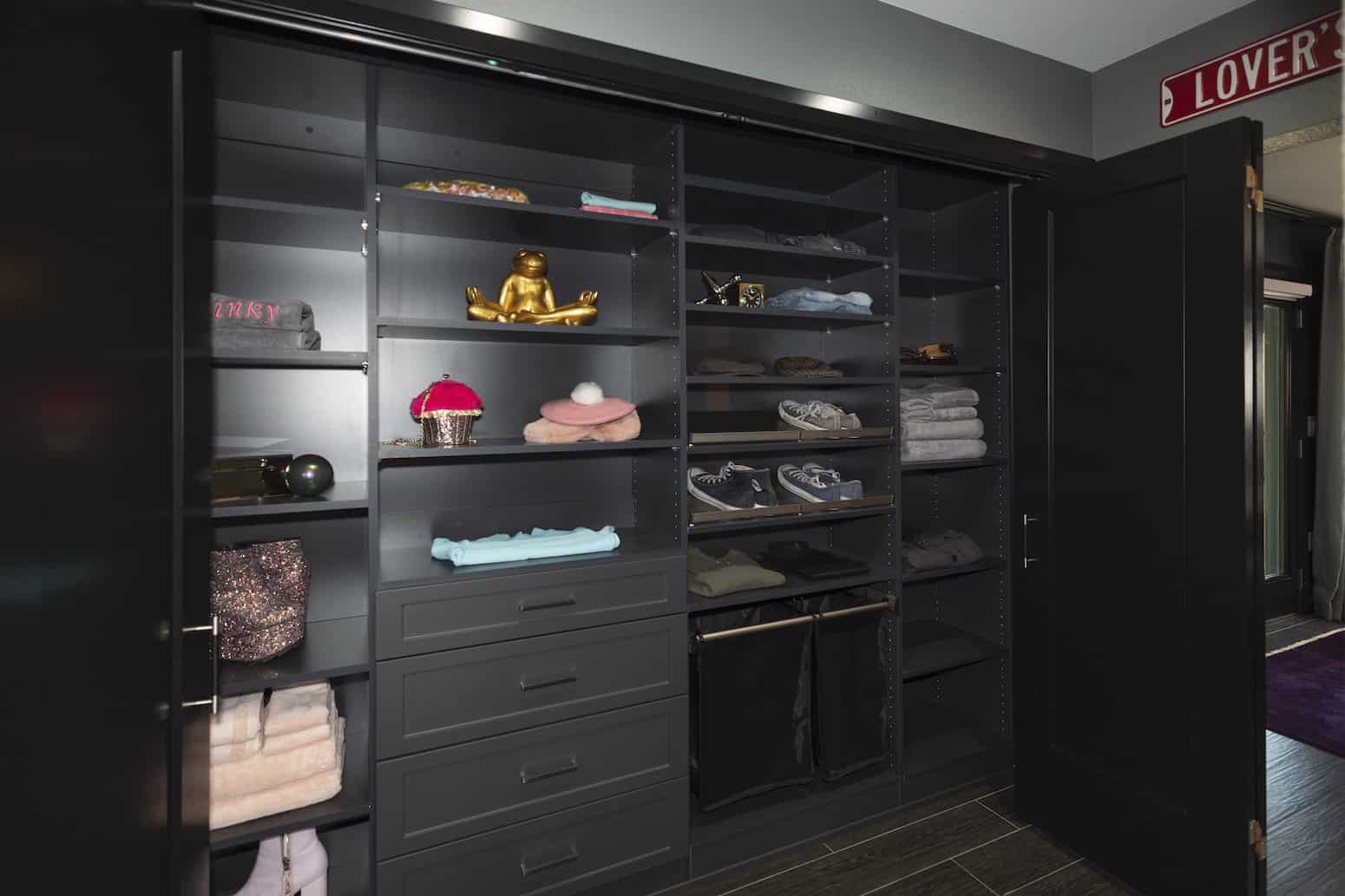 Black walk-in closet with open shelving, drawers, neatly folded clothes, and shoes