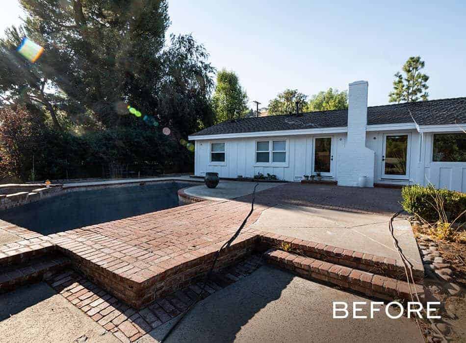 Outdoor view of a backyard pool area with a drained pool, surrounded by brick and concrete decking