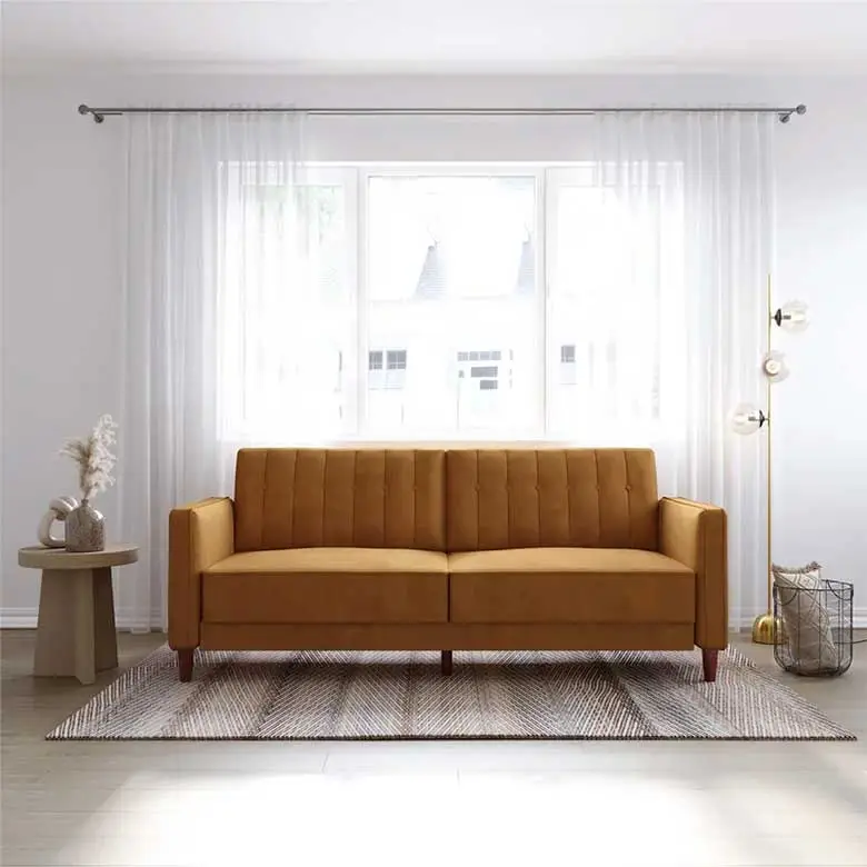 A mustard yellow velvet sofa with a tufted design, sitting in front of a large window with white curtains