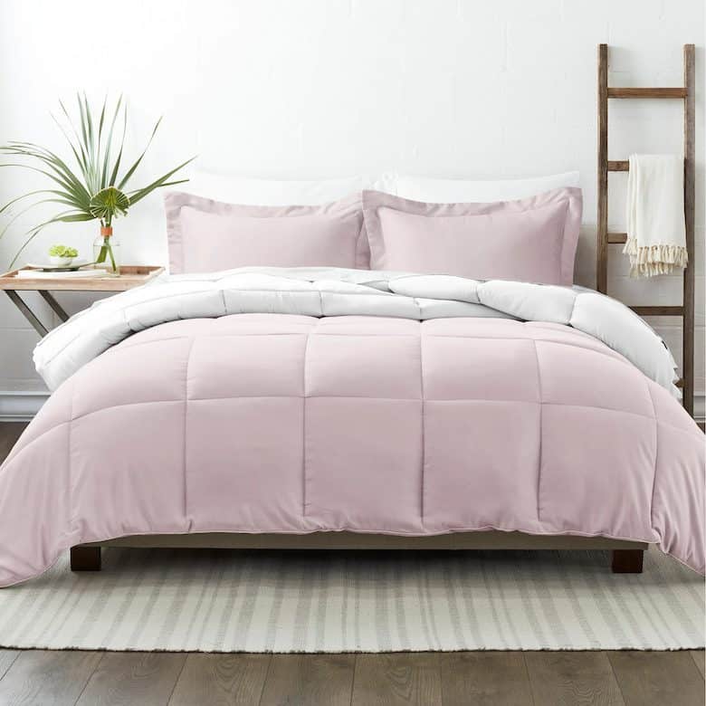 A neatly made bed with a light pink comforter, matching pillows, and a white duvet