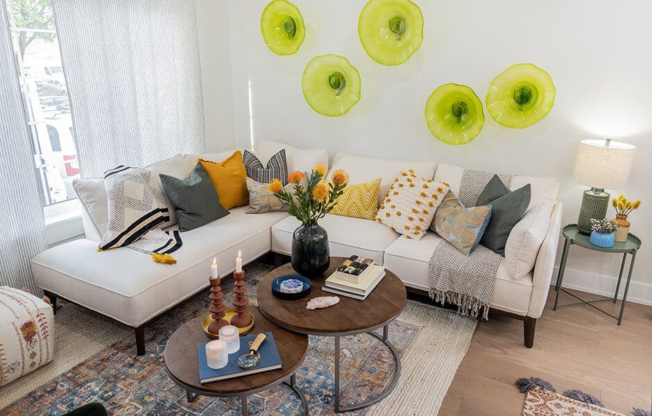 Bright and colorful living room with a white sectional sofa, decorative green wall art, and round wooden coffee tables