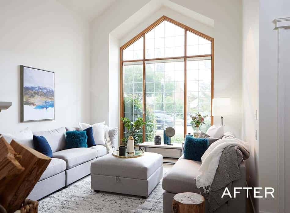 Bright living room with large arched window, gray sectional sofa, blue accents, and a central ottoman