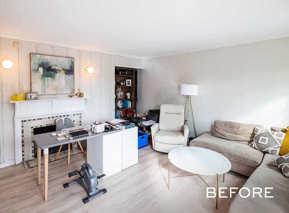 A before image of a living room with a workspace, neutral sofa, recliner, fireplace, and cluttered desk