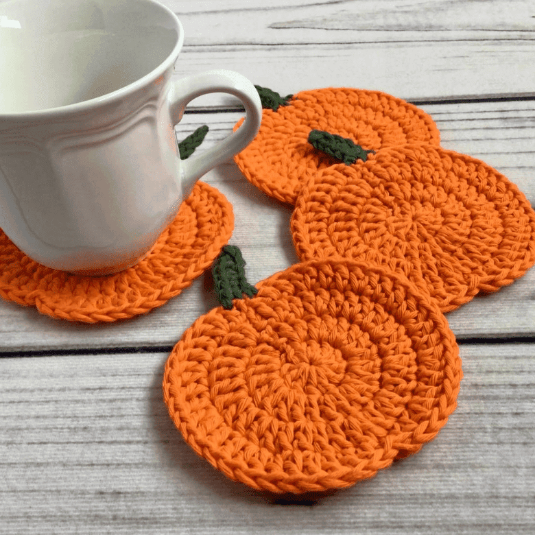 Handmade crochet pumpkin coasters in orange with green stems on wooden surface