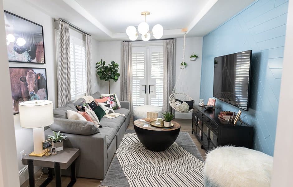 Cozy living room with a gray sectional sofa, blue accent wall, wall-mounted TV, and a hanging chair by French doors