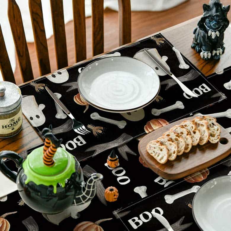 Halloween-themed table setting with spooky placemats, a witch cauldron teapot, and a breadboard
