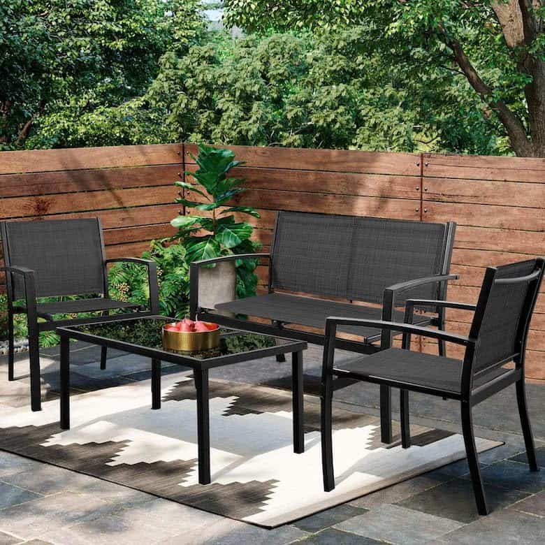 Outdoor patio set with black metal chairs, a matching table, a geometric rug, and wooden fencing