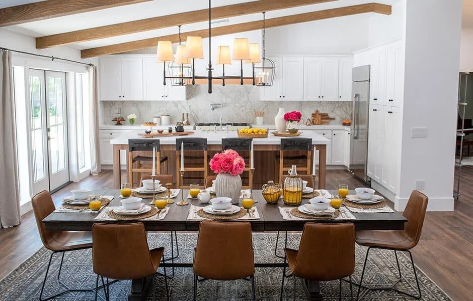 Dining area with a rustic table, leather chairs, and a bright kitchen with white cabinets and wood beams