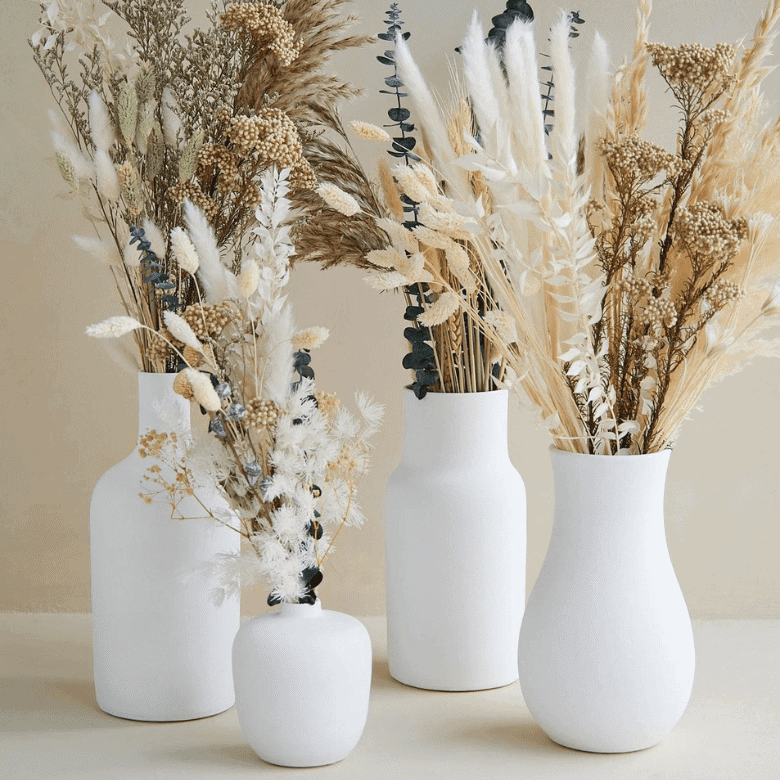 Four white vases with various dried floral arrangements