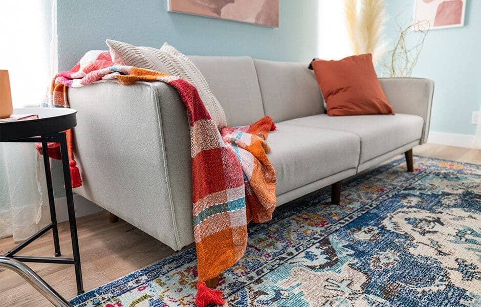 Cozy living room with a gray sofa, colorful throw blanket, and patterned blue rug