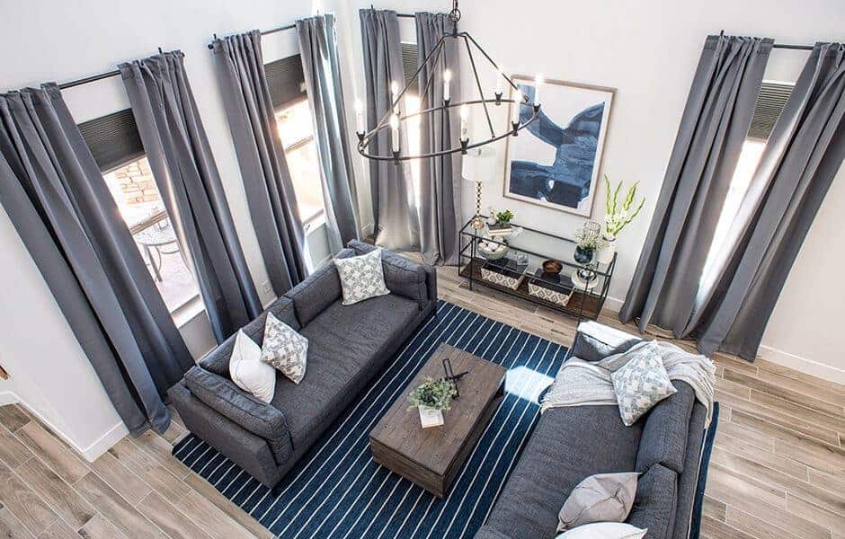 Modern living room with tall ceilings, large windows, gray curtains, chandelier, sofas, coffee table, rug, console table, and painting