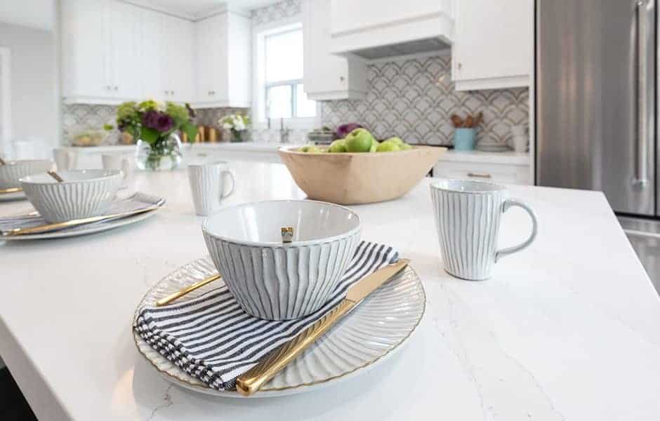 A kitchen countertop featuring a set of white dishes with gold rims