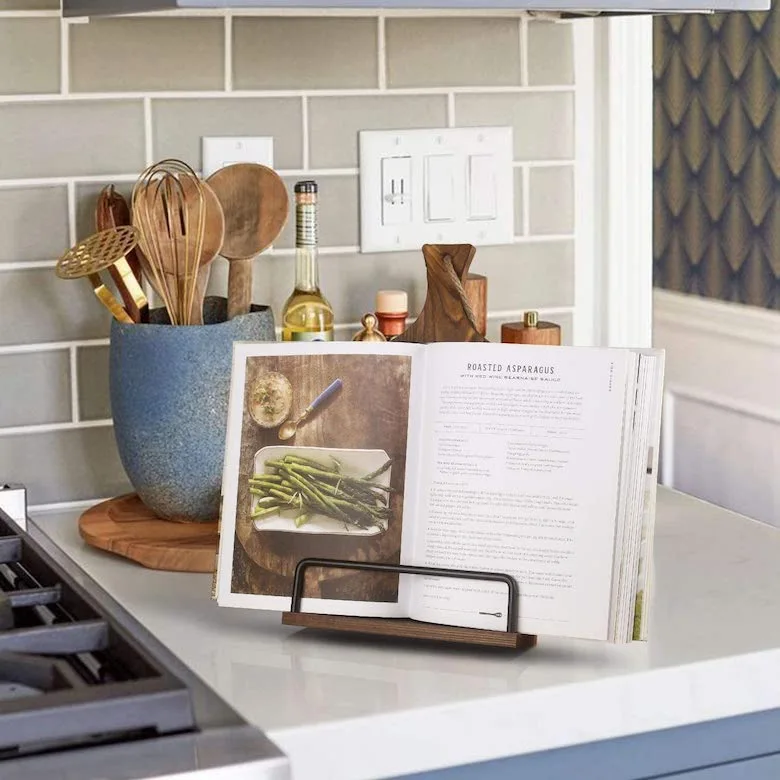 Cookbook on stand with wooden utensils on kitchen counter