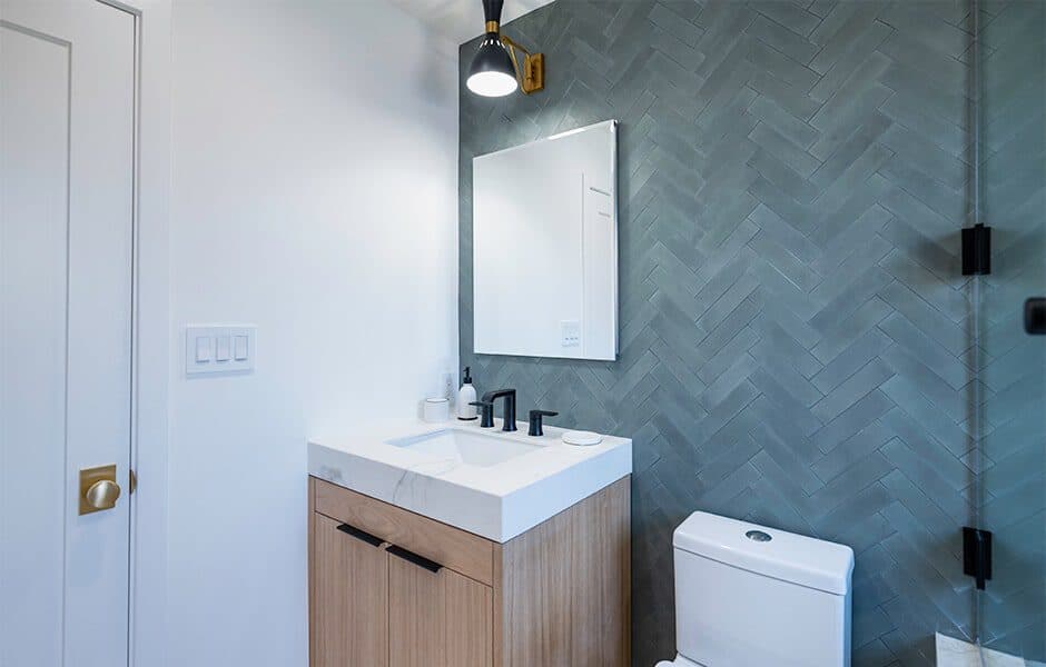 Bathroom with herringbone tile wall, wood vanity, and black fixtures