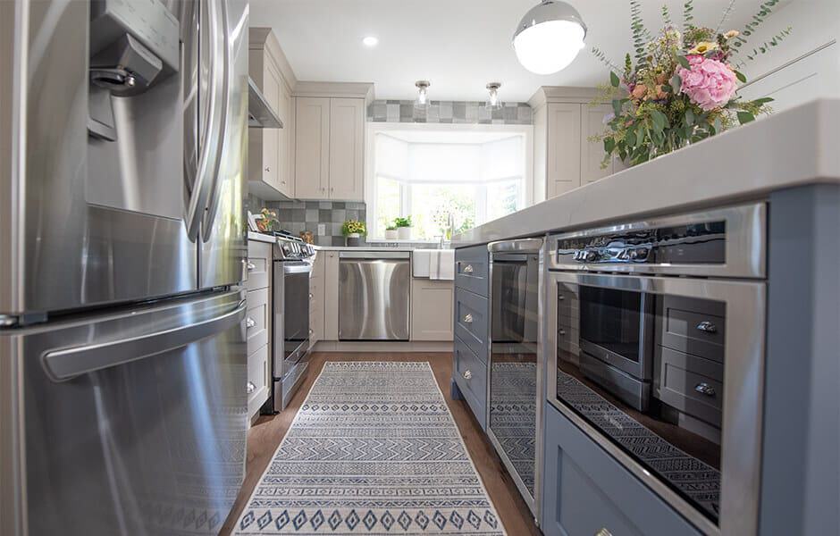 Kitchen with stainless steel appliances, a blue island, and a patterned runner rug