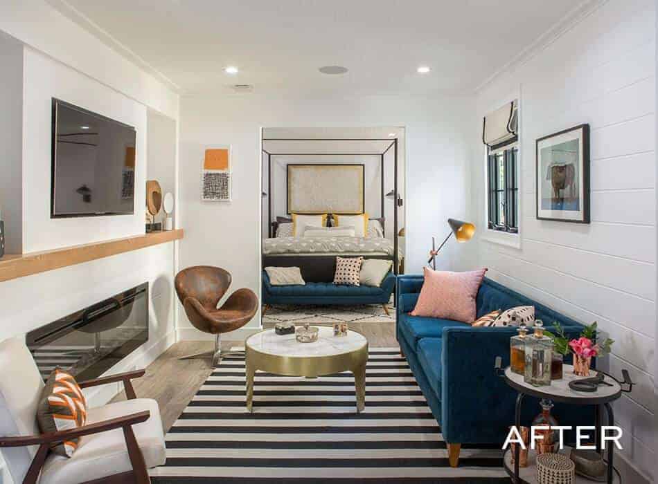 Modern living room with blue sofa, striped rug, wall-mounted TV, and a view of a canopy bed