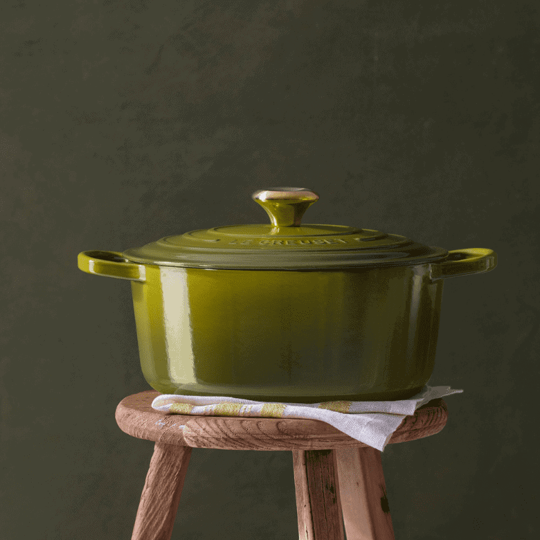 Green cast iron Dutch oven placed on a rustic wooden stool