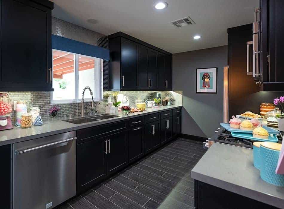 Modern kitchen with dark cabinets, light countertops, a tiled backsplash, and colorful desserts on display