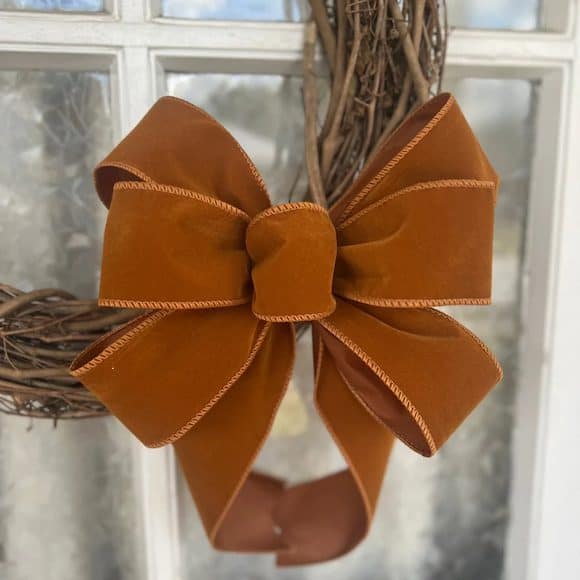 Rust velvet bow on grapevine wreath hanging on glass door