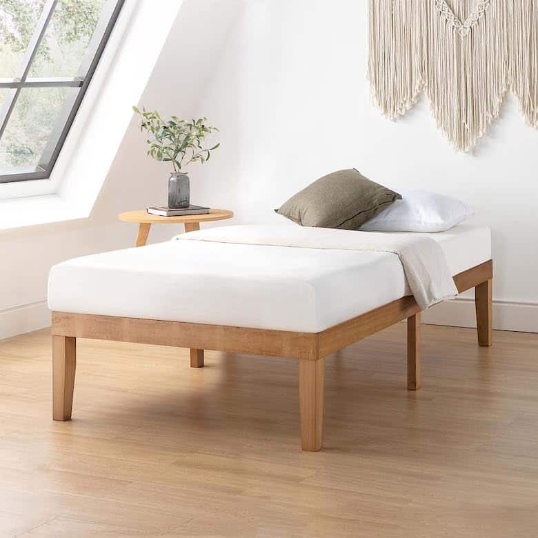 Minimalist bedroom with a wooden bed frame, white bedding, a side table, and a macrame wall hanging
