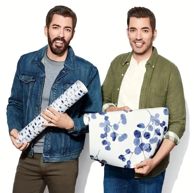 Drew and Jonathan Scott stand together holding pieces of peel and stick wallpaper