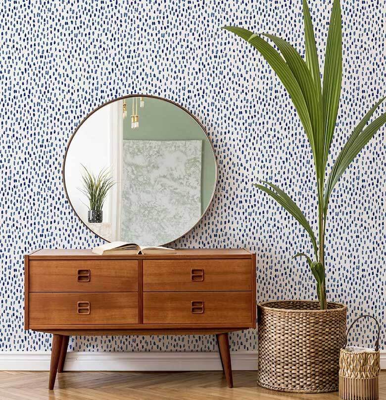 Sideboard and mirror sit against a wall with blue and white wallpaper
