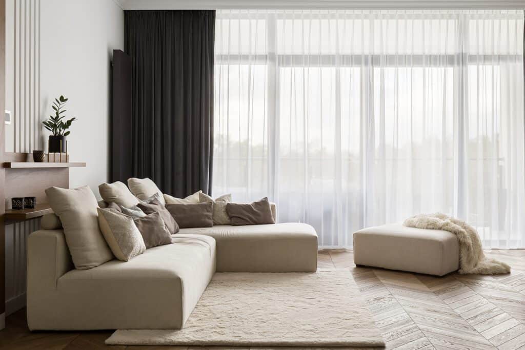 cozy neutral sofa in front of big window with ottoman and faux fur blanket