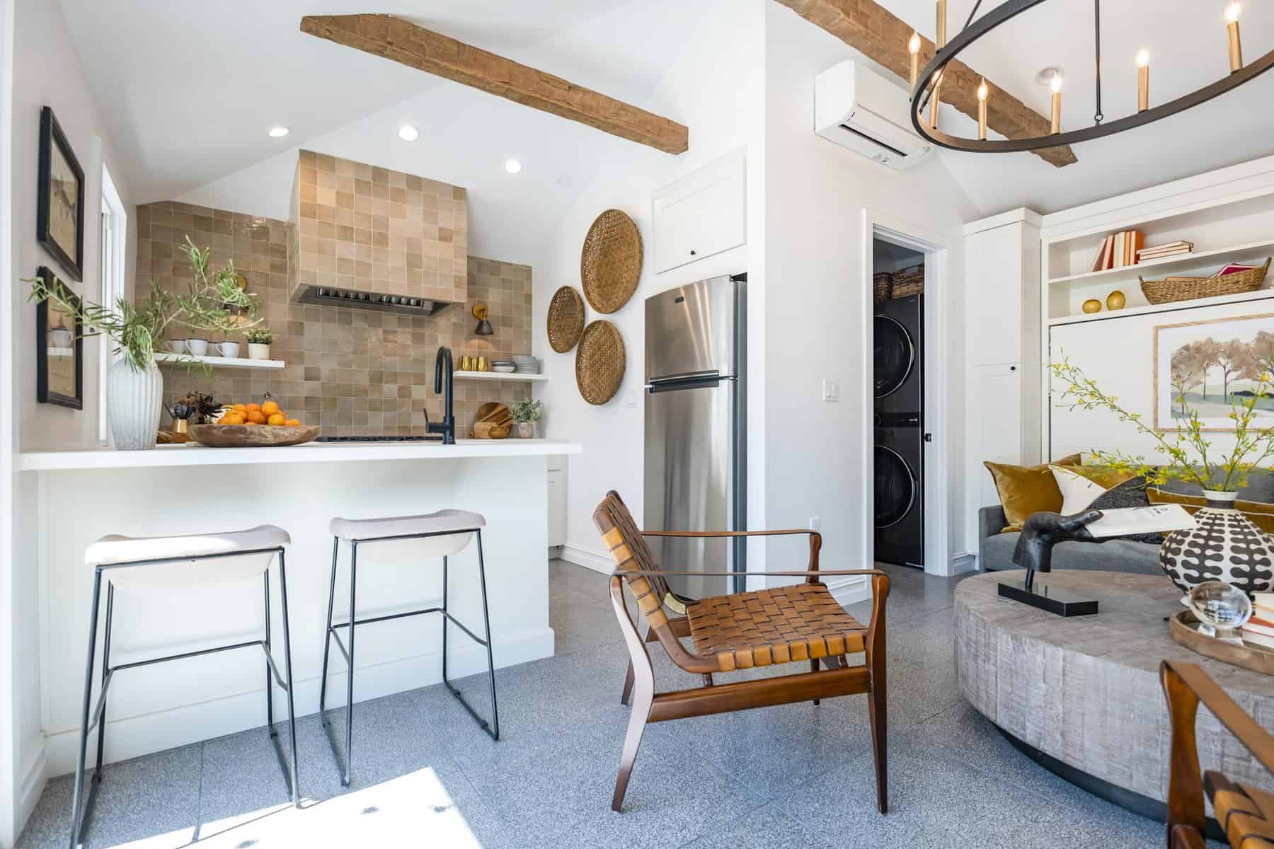 Bright, modern kitchen and living space with wood beams, bar stools, woven decor, a stainless steel fridge, and cozy seating