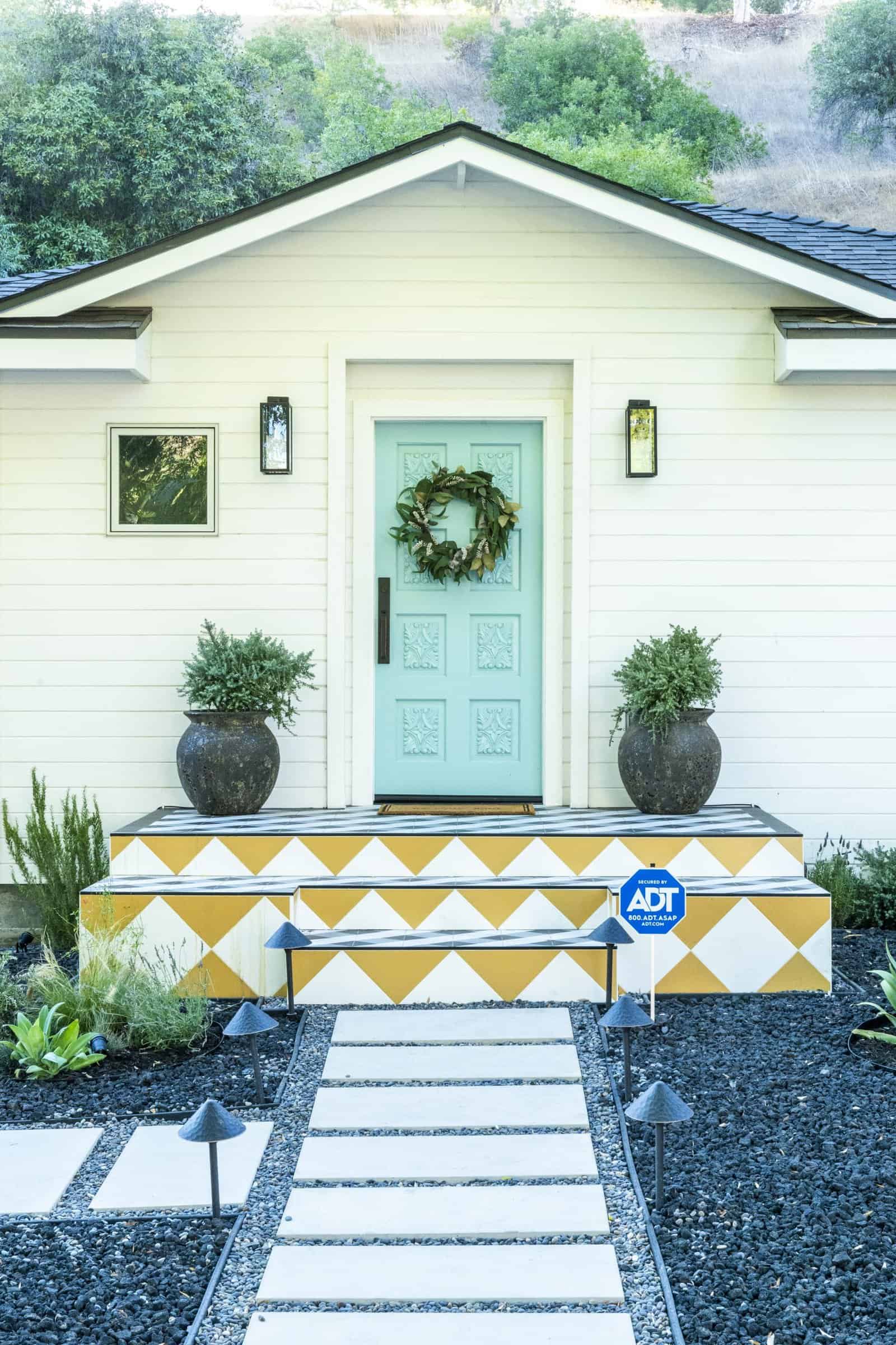 Charming front porch with light blue door, geometric tile steps, potted plants, and stone path walkway