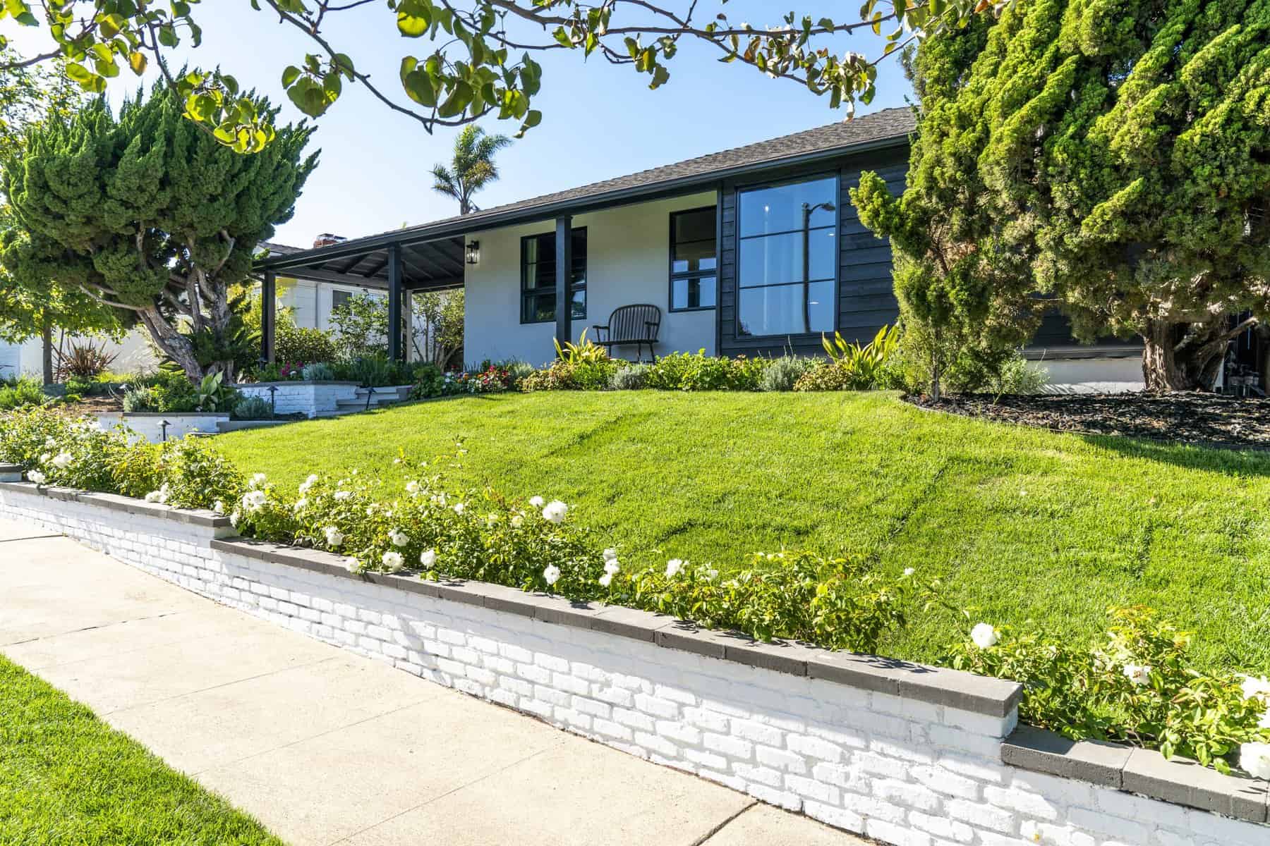 Modern home with a landscaped front yard, black accents, and lush greenery
