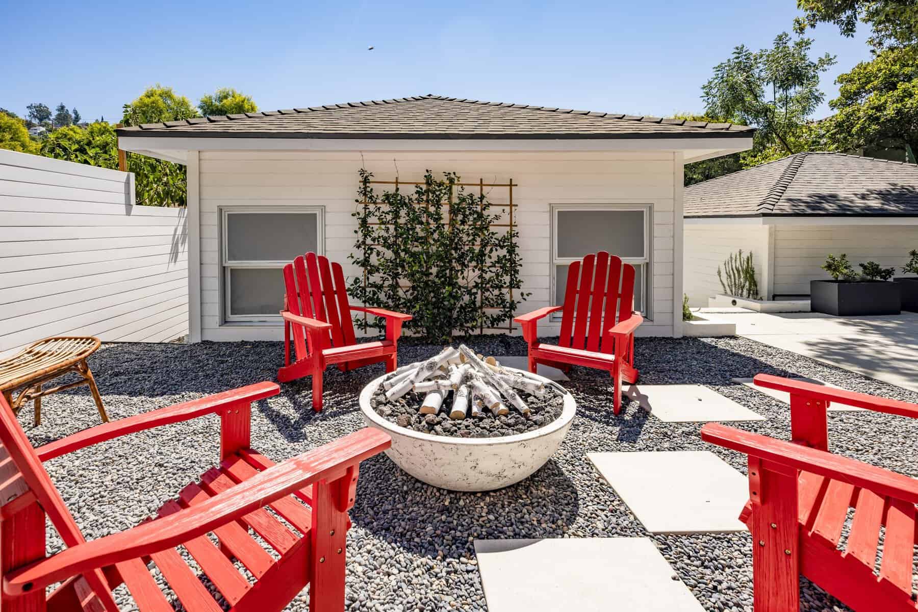 Patio with red Adirondack chairs, a fire pit, and a white guesthouse